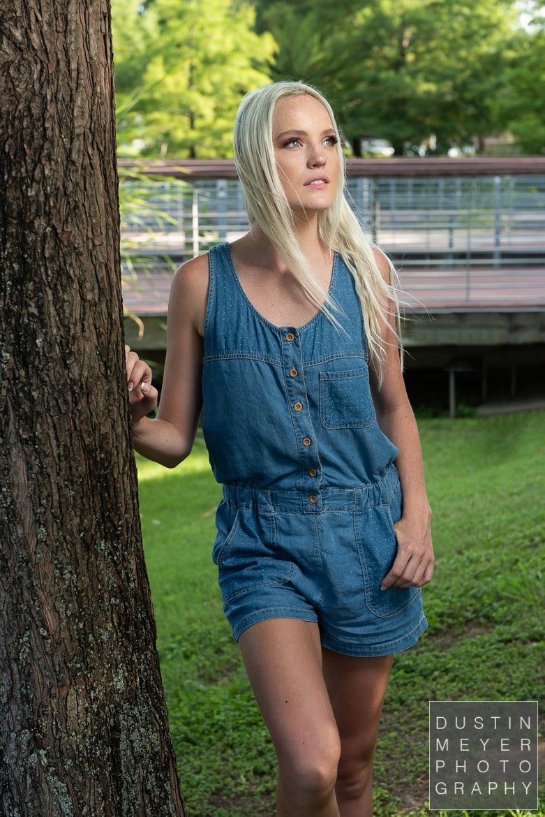 a model headshot of a female with blonde hair and a denim romper taken outdoors