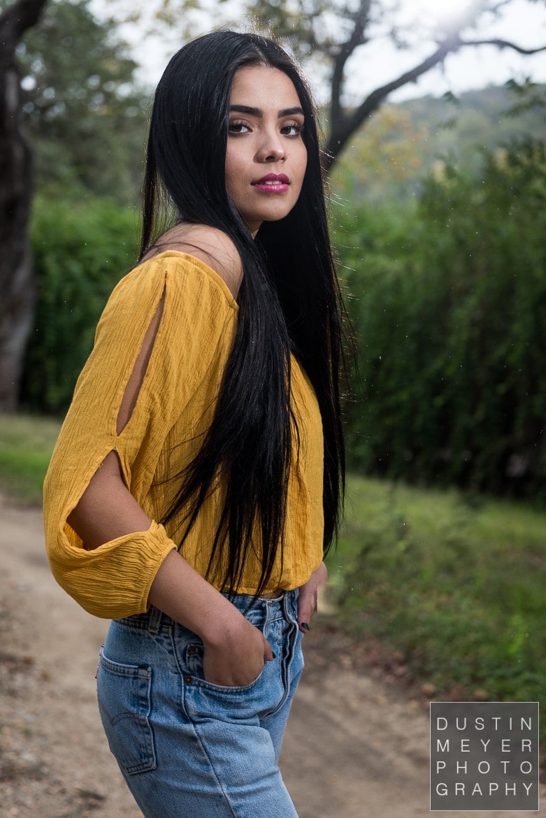 a female model with black hair outdoors wearing a yellow shirt and jeans